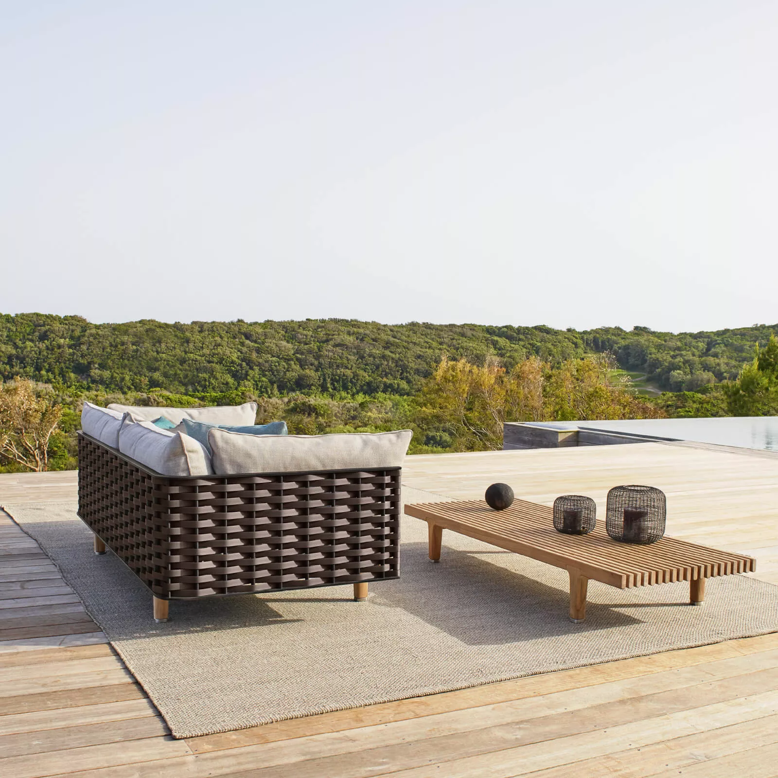 Dedon Sealine Sofa von Jean Marie Massaud auf einer Terrasse mit Blick auf bewaldete Hügel und einem niedrigen Holztisch mit Dekoration