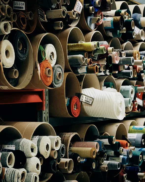 Stoffrollen in verschiedenen Farben und Texturen in einem Lagerregal, fotografiert aus der Seitenperspektive.