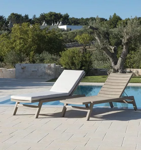 Zwei Ethimo Costes Sonnenliegen aus gebeiztem Teakholz, eine mit weißem Polster, stehen nebeneinander auf einer Terrasse am Pool.