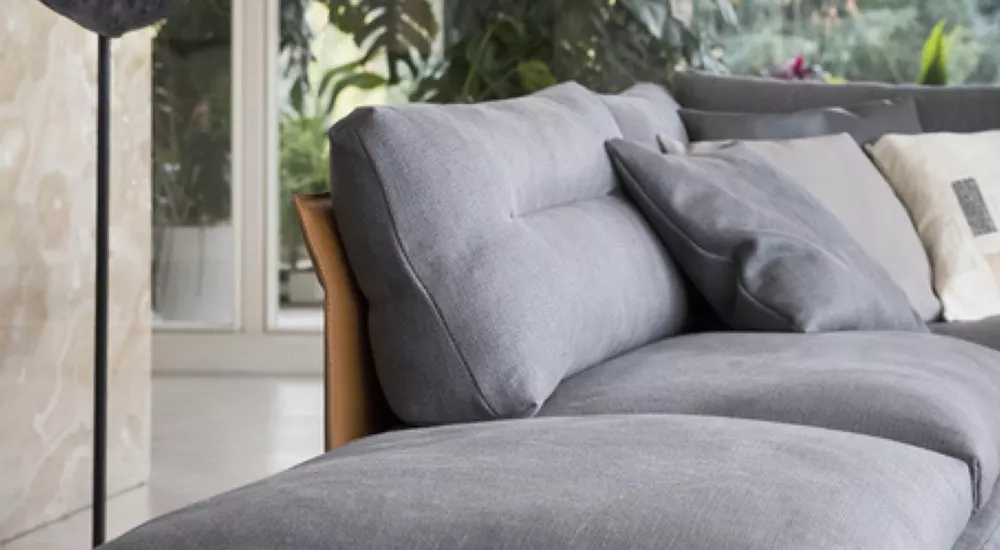 Poltrona Frau Gran Torino Sofa in Grau, Nahaufnahme in modernem Wohnzimmer mit großen Fenstern und Pflanzen im Hintergrund.