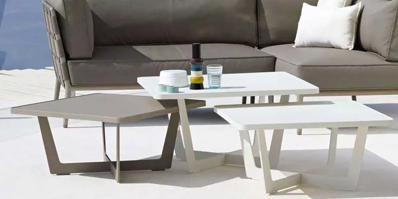 Cane-line Time-Out Beistelltische in Weiß und Grau auf einer Terrasse vor einem grauen Sofa, stimmungsvolles Outdoor-Setting.