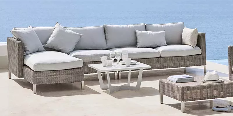 Cane-line Connect Loungegruppe in Grau auf einer Terrasse mit Meerblick, bestehend aus Sofa, Tisch und Hocker, in entspannter Atmosphäre.