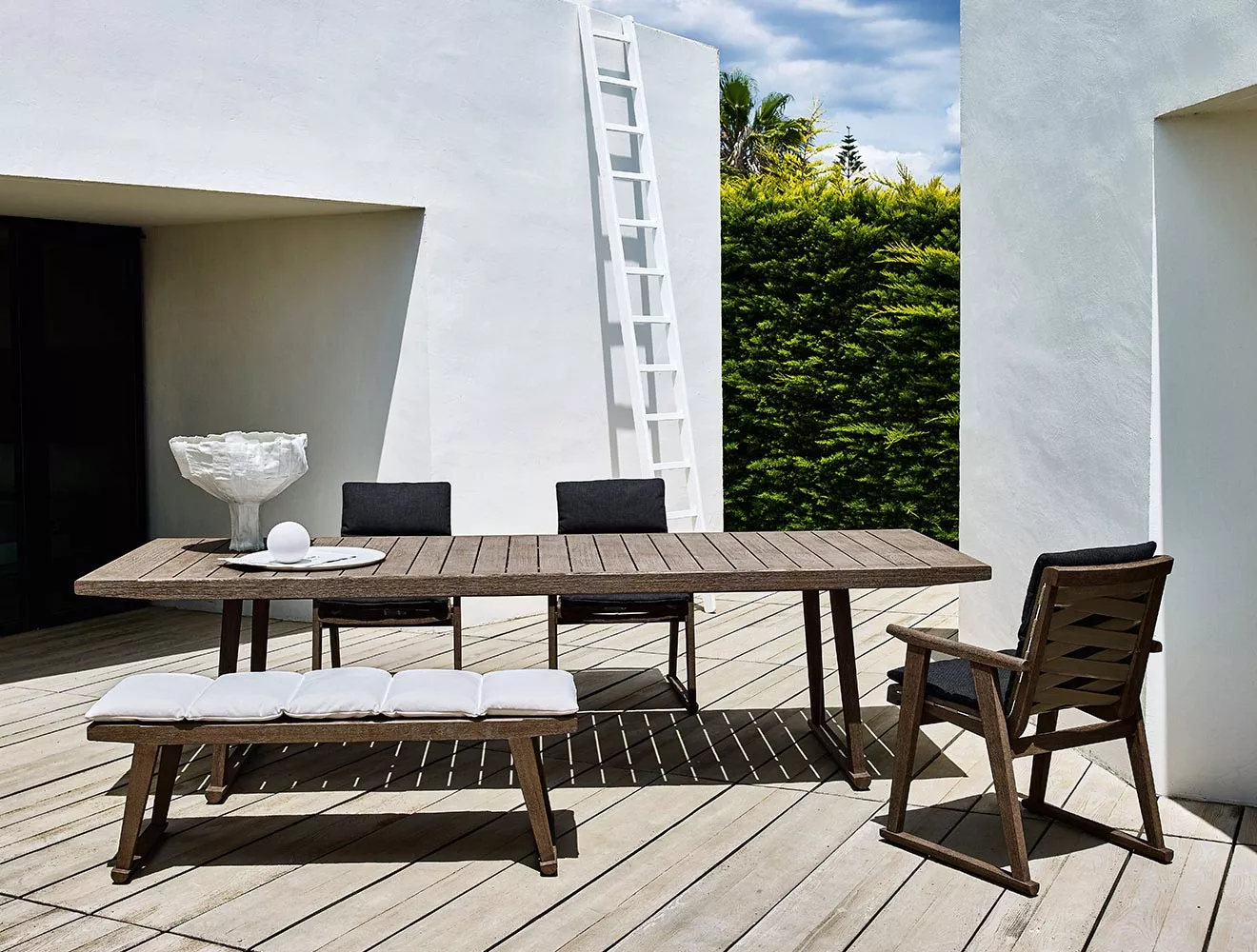 B&B Italia Gio Gartentisch 220 cm auf einer Terrasse mit Stühlen und Bank im modernen Design bei sonnigem Wetter und grüner Hecke im Hintergrund