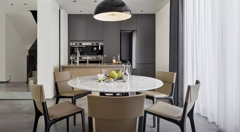 Esszimmer mit Poltrona Frau Isadora Stühlen in Beige um einen runden Marmortisch, moderne Küche im Hintergrund, helle Atmosphäre.