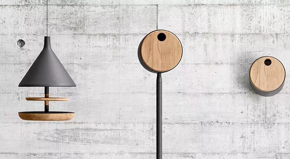 Gloster Accessoires in Grau und Holzoptik vor einer Betonwand, bestehend aus einem hängenden und zwei wandmontierten Elementen.