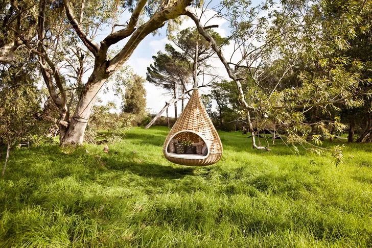 Nestrest Hanging Lounger rund 200 cm von Dedon hängt an einem Baum in einer grünen Wiese umgeben von Bäumen und Pflanzen