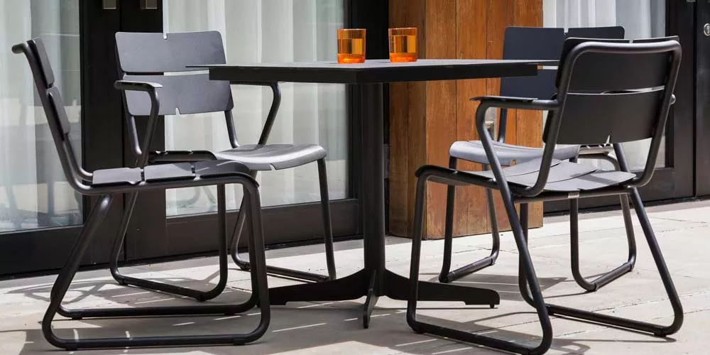 Oasiq Ceru Essgruppe in Anthrazit auf einer Terrasse, bestehend aus einem quadratischen Tisch und vier Stühlen mit Armlehnen.