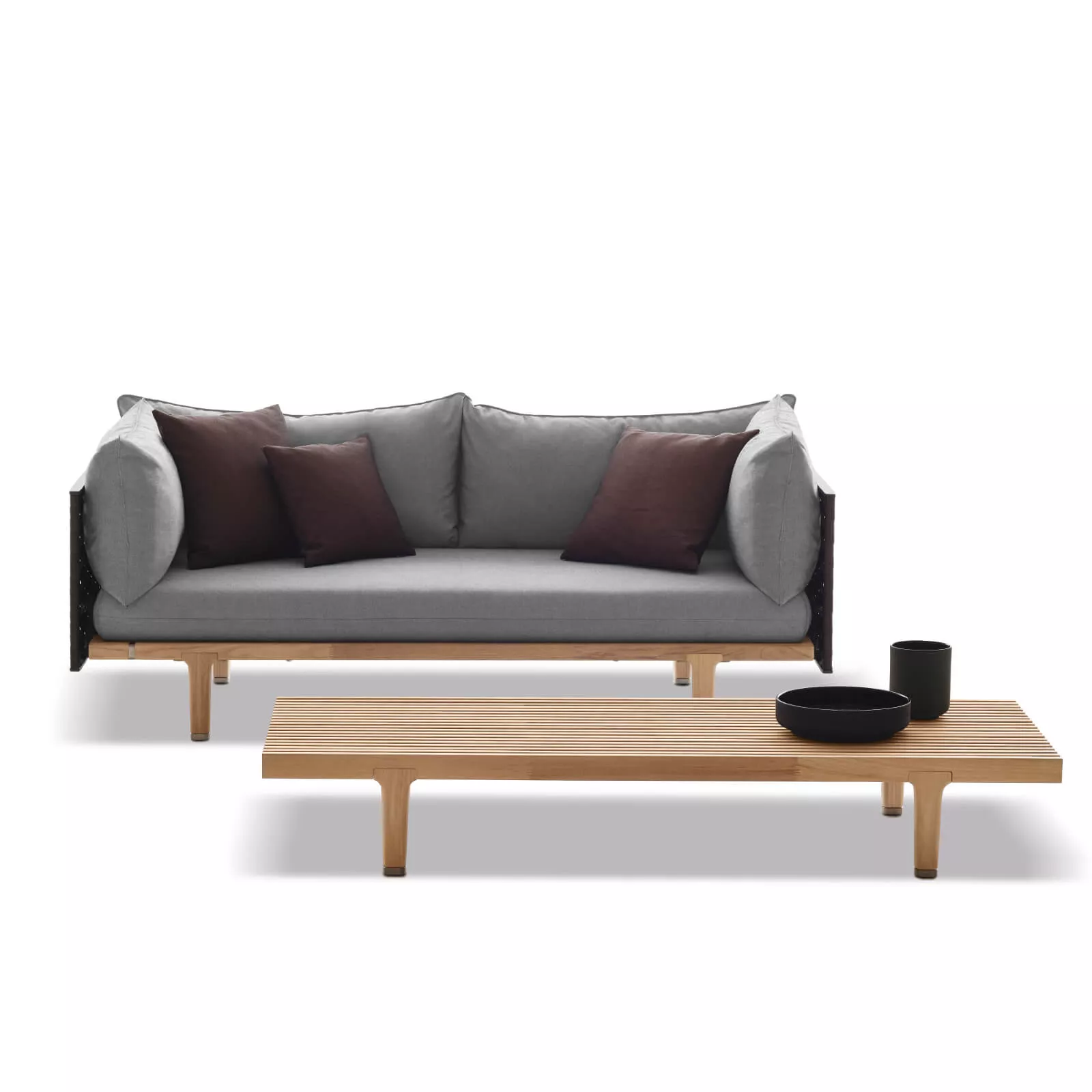 Dedon Sofa mit grauen Kissen und braunen Akzenten vor einem niedrigen Holztisch mit schwarzen Schalen ohne Hintergrund