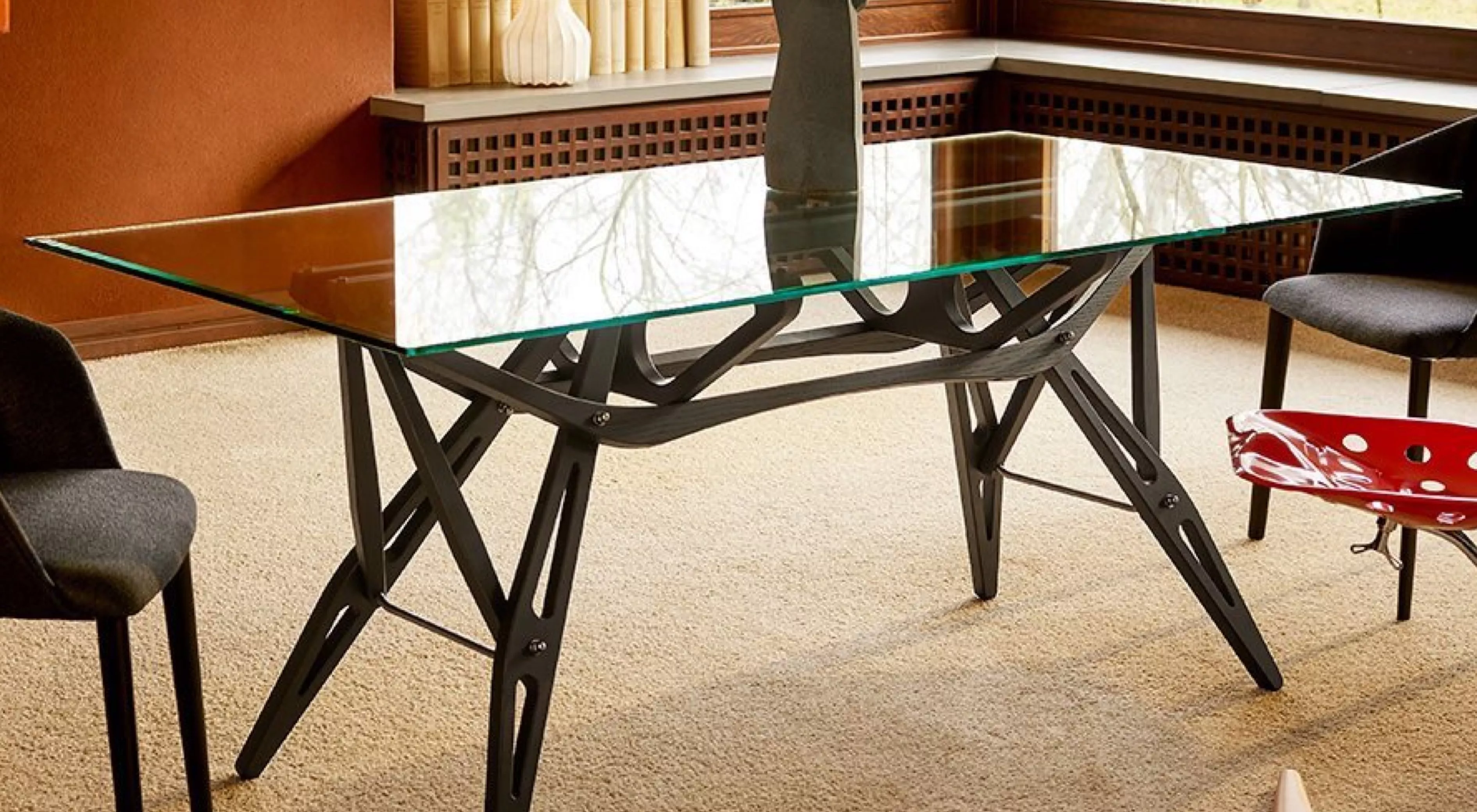 Ein moderner Glas-Esstisch von Reale in einem gemütlichen Wohnzimmer mit Teppichboden und Stühlen im Hintergrund.