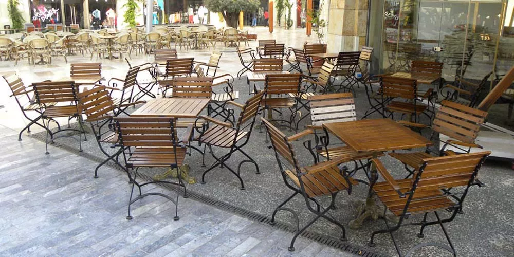 Außenbereich mit Royal Mirage Vienna Gartenmöbeln aus braunem Holz und schwarzem Metall auf grauem Steinboden, stimmungsvolle Atmosphäre.
