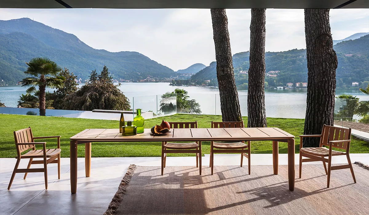 Roda Essplatz aus hellem Holz auf Terrasse mit Seeblick, umgeben von grüner Landschaft und Bergen, stimmungsvolles Ambiente.