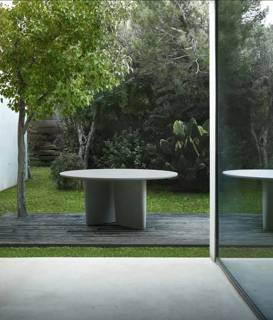 B&B Italia Tobi Ishi Outdoor Esstisch 162 cm steht auf einer Terrasse im Garten neben einem Baum und spiegelt sich in einer Glaswand