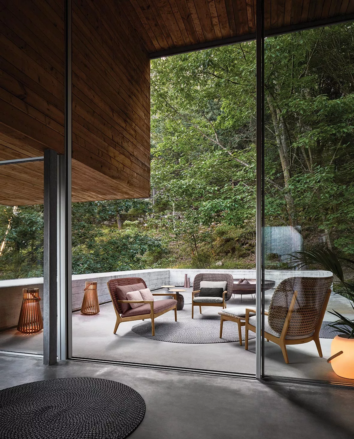 Gloster Kay Loungegruppe in Naturtönen auf einer Terrasse mit Waldblick, umgeben von Holz- und Glasarchitektur.
