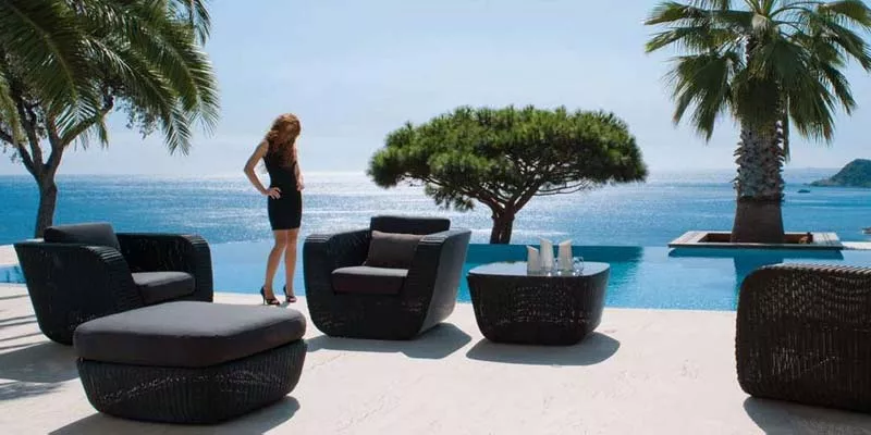 Cane-line Savannah Loungegruppe in Schwarz auf einer Terrasse mit Meerblick, bestehend aus Sesseln, Tisch und Hocker, stimmungsvolle Szene.