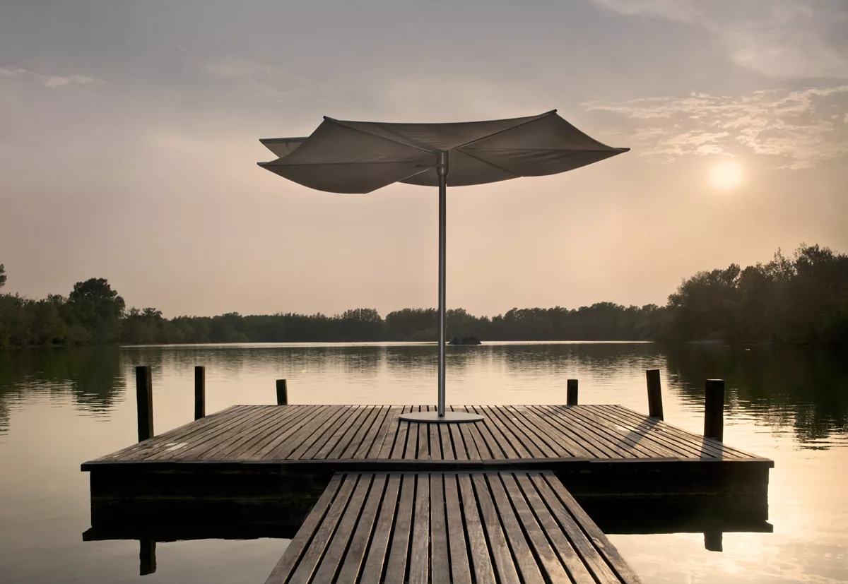 Calma OM Sonnenschirm aus eloxiertem Aluminium, 300 cm, auf einem Holzsteg am See bei Sonnenuntergang.