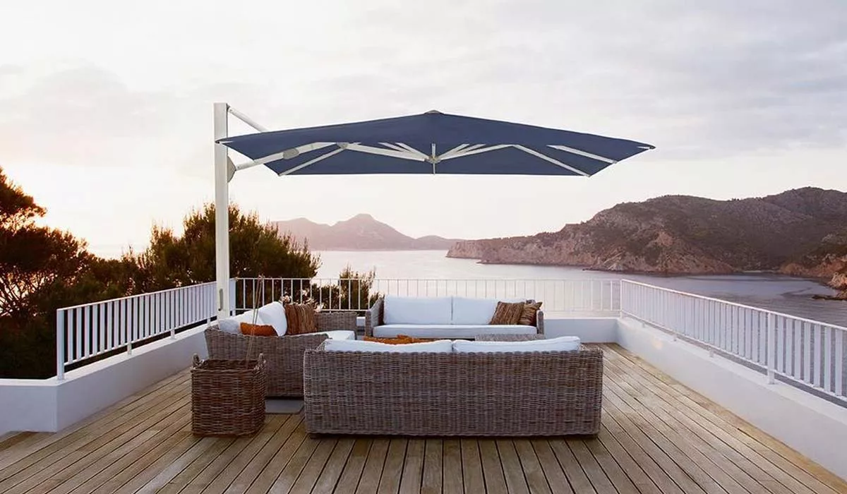 Glatz Freiarm-Sonnenschirm in Blau auf einer Terrasse mit Meerblick und Loungemöbeln bei Sonnenuntergang.