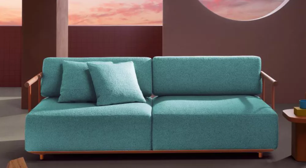 Sofa Pedrali in Türkis auf einer Terrasse bei Sonnenuntergang, mit zwei passenden Kissen, vor einer runden Fensteröffnung.