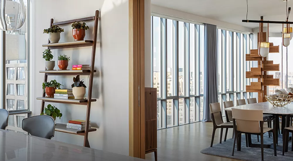 Moderne Wohnung mit großen Fenstern, Holzmöbeln und Pflanzen, die eine helle und einladende Atmosphäre schaffen.