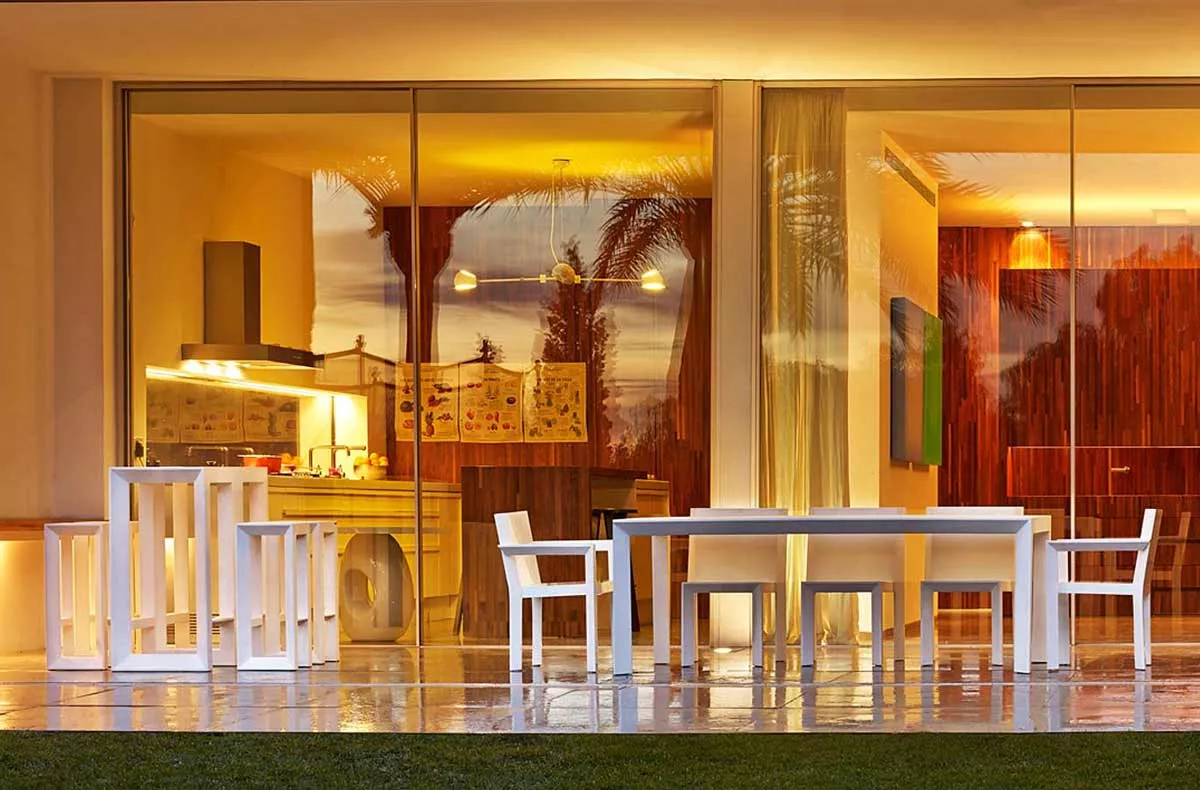 Vondom Frame Essgruppe in Weiß auf einer Terrasse vor einer modernen Glasfassade bei Sonnenuntergang.