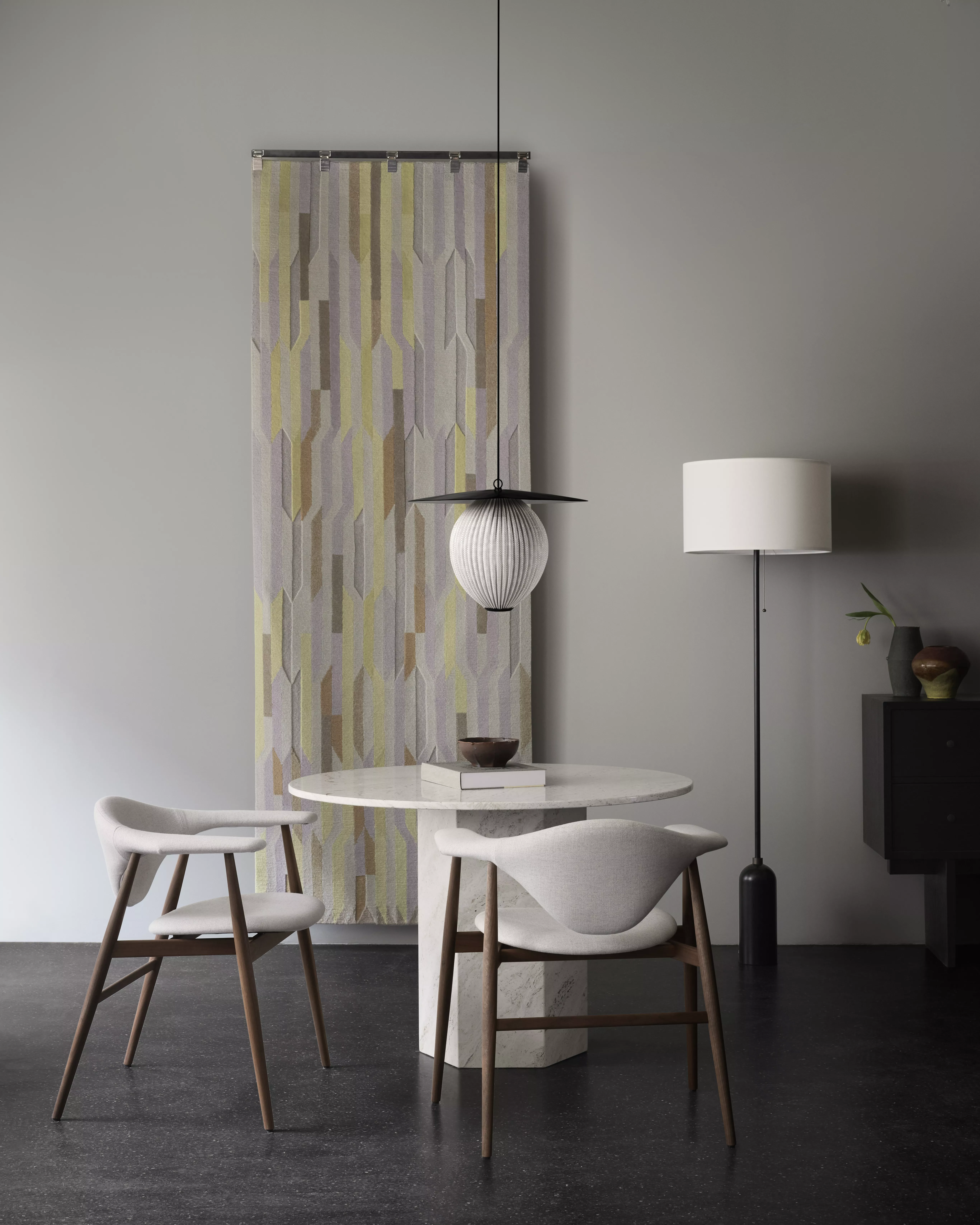 Ein stilvolles Wohnzimmer mit Gubi Masculo Stühlen einem runden Tisch einer Stehlampe und einer modernen Wanddekoration im Hintergrund.