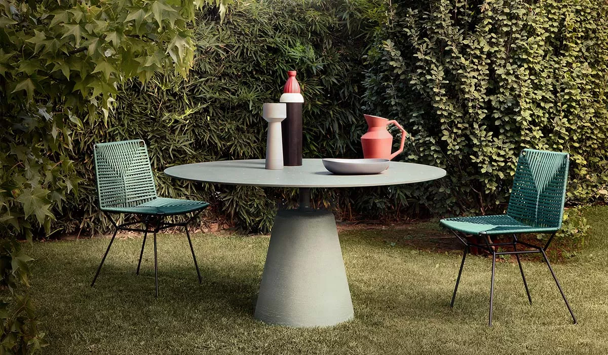 MDF Italia Tisch und Stühle in Grün auf Rasen, umgeben von Pflanzen, mit Keramikdekorationen auf dem Tisch, stimmungsvolle Gartenaufnahme.