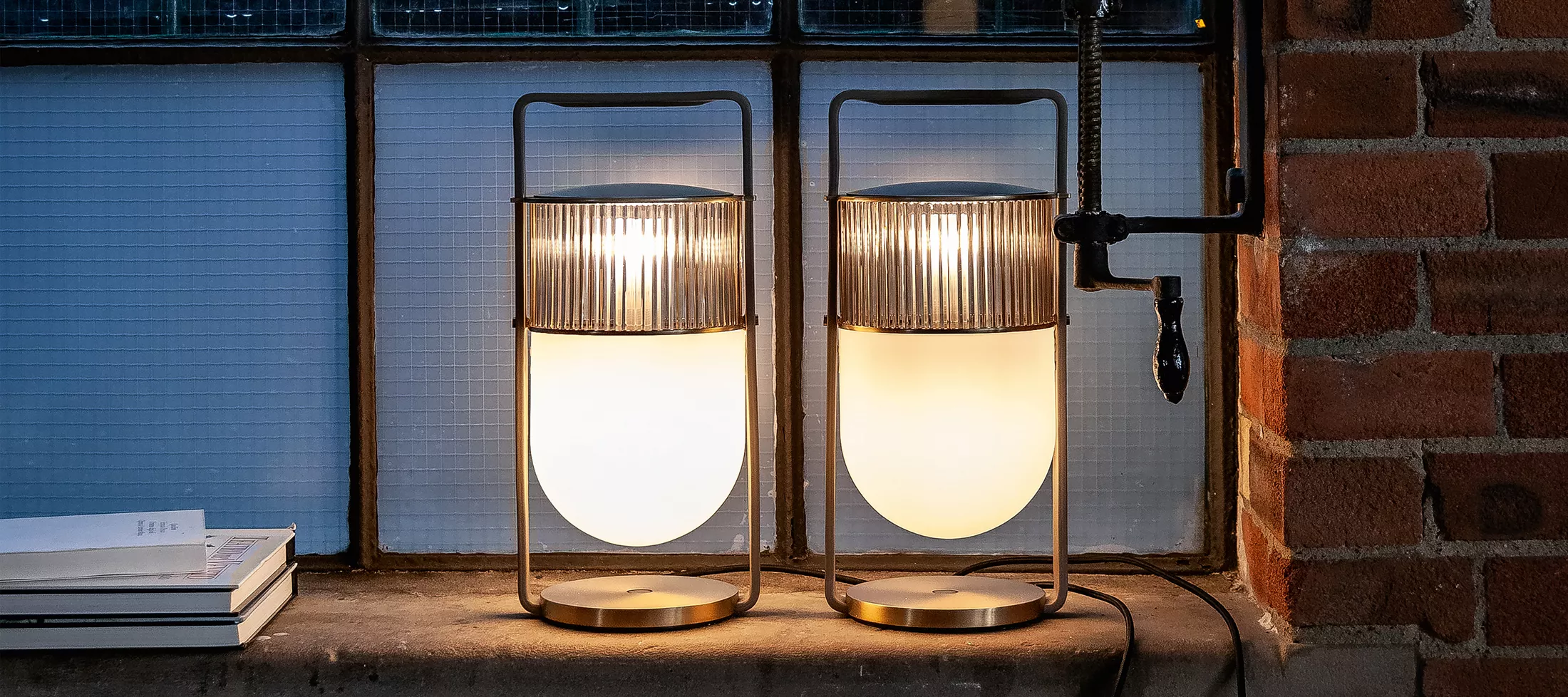 Zwei Poltrona Frau Leuchten in warmem Licht auf einer Fensterbank vor einer Backsteinwand, stimmungsvolle Abendatmosphäre.