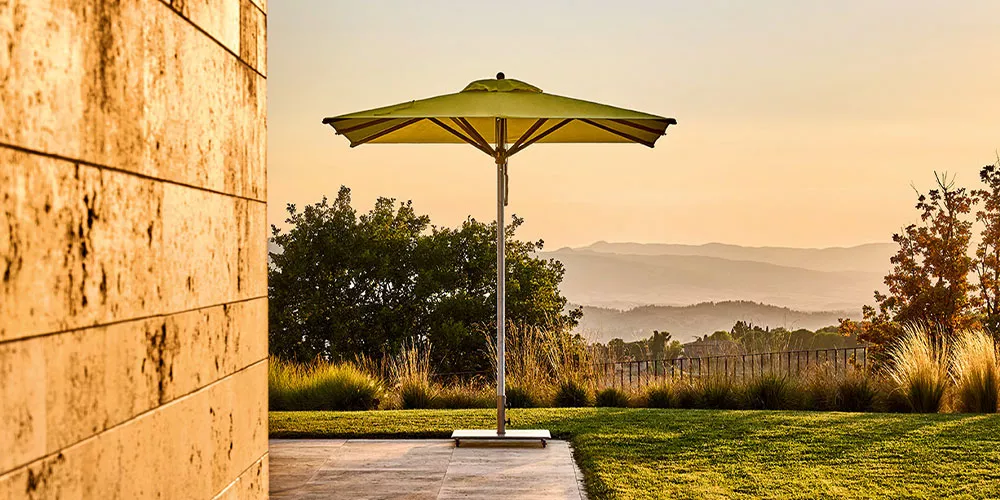 Weishäupl Trend Sonnenschirm in Grün auf einer Terrasse mit Blick auf eine hügelige Landschaft bei Sonnenuntergang.