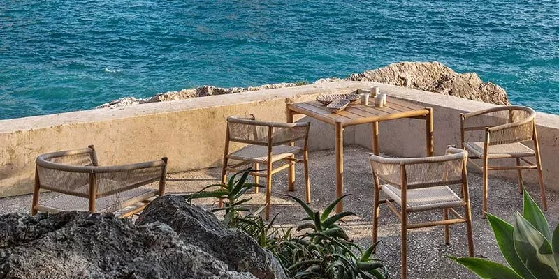 Ethimo Kilt Outdoor Essgruppe in Naturtönen auf einer Terrasse mit Meerblick, bestehend aus einem Tisch und vier Stühlen.