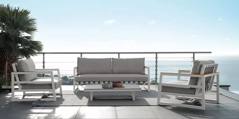 Talenti Kollektion Alabama, graue Outdoor-Möbelgarnitur auf Terrasse mit Meerblick, bestehend aus Sofa, zwei Sesseln und Tisch.