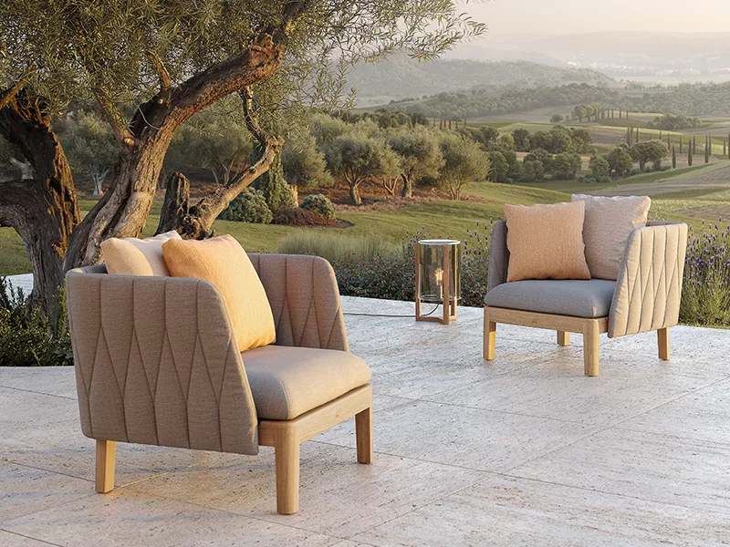 Calypso Loungesessel in Beige auf einer Terrasse mit Blick auf eine mediterrane Landschaft bei Sonnenuntergang.