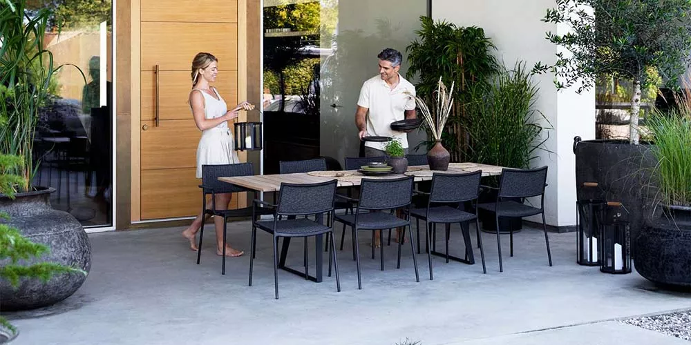 Caneline Less Kollektion, schwarzer Tisch und Stühle, Outdoor-Setting, moderne Terrasse mit Pflanzen im Hintergrund.