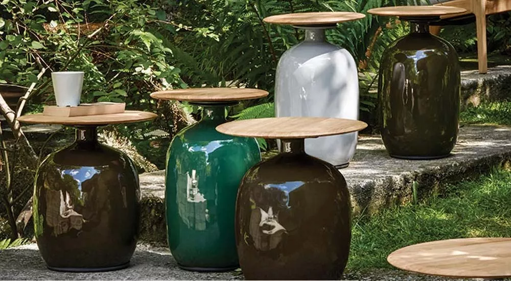 Gloster Blow Beistelltische in Grün, Braun und Weiß auf einer Terrasse im Garten, mit Holzplatten und einer Tasse auf einem Tisch.