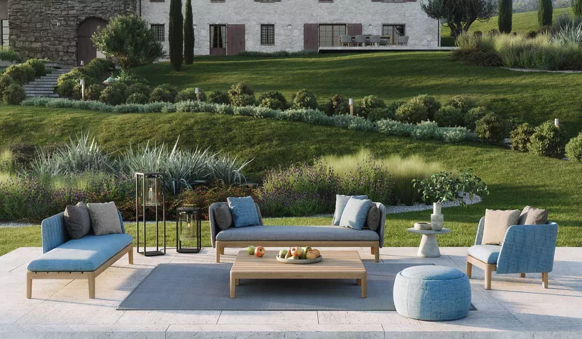 Royal Botania Calypso Loungegruppe in Blau auf einer Terrasse mit Blick auf einen gepflegten Garten und ein Landhaus im Hintergrund.