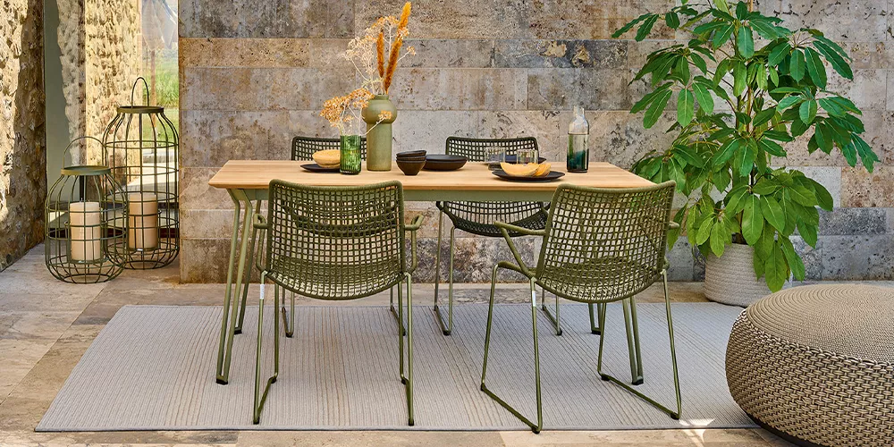 Weishäupl Slope Gartenmöbel-Set in Olivgrün auf einer Terrasse mit Steinwand und Pflanzen im Hintergrund.