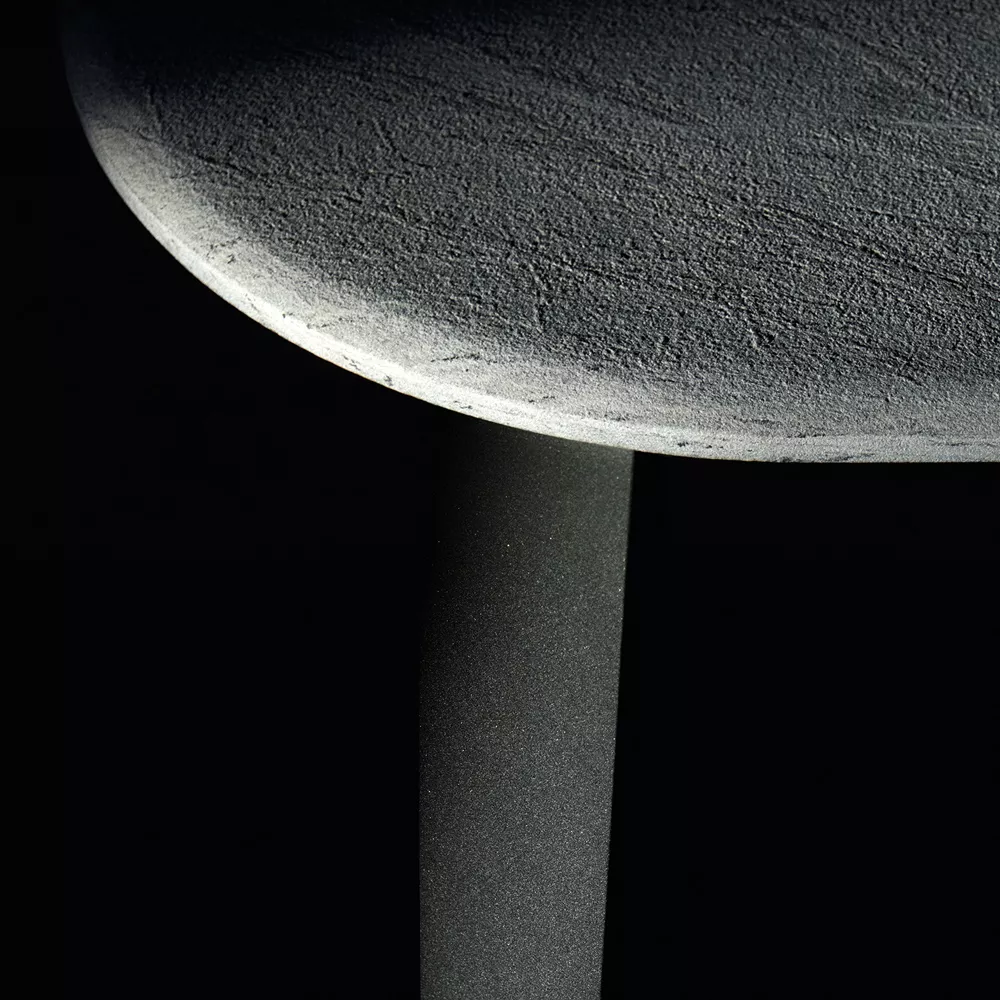 B&B Italia Ginepro Tisch zeigt eine Nahaufnahme der Tischkante und des Tischbeins in einem stimmungsvollen Bild mit dunklem Hintergrund