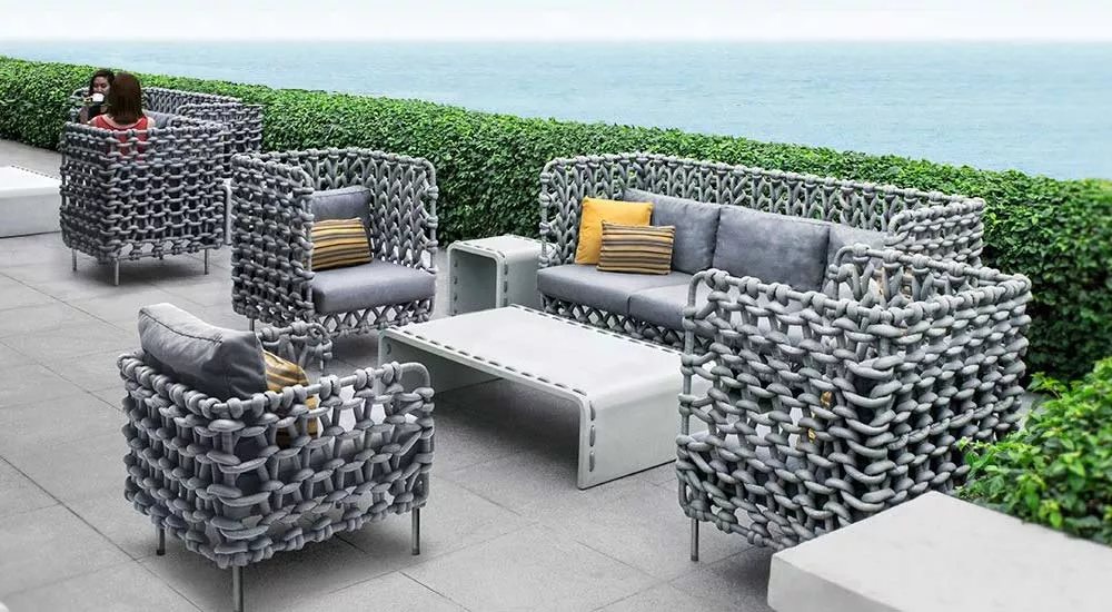 Kenneth Cobonpue Cabaret Loungegruppe in Grau auf einer Terrasse mit Meerblick, bestehend aus Sofas und Sesseln, umgeben von Hecken.