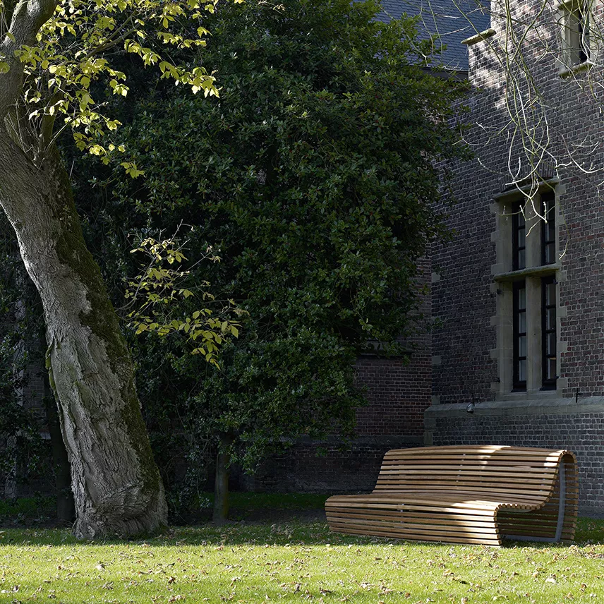 B&B Italia Titikaka Gartenbank steht auf einer grünen Wiese neben einem Baum und einem Backsteingebäude im Hintergrund