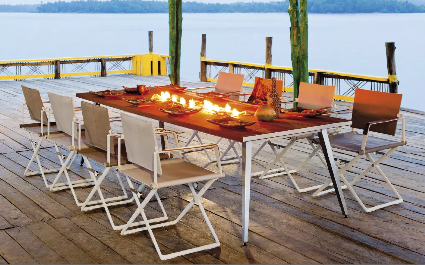 Dedon Seax Armlehnstuhl aus der Seax Kollektion auf einer Terrasse an einem Esstisch mit brennenden Kerzen und gedecktem Tisch am See