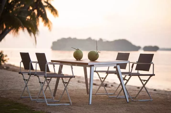 Dedon Seax Kollektion Seax Armlehnstuhl klappbar am Strand mit Tisch und zwei Kokosnüssen im Sonnenuntergang