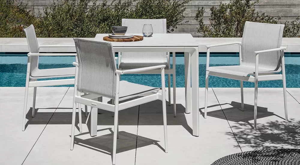 Gloster 180 Gartenmöbel Essgruppe in Weiß vor einem Pool auf einer Terrasse, bestehend aus einem Tisch und vier Stühlen, in sommerlicher Atmosphäre.