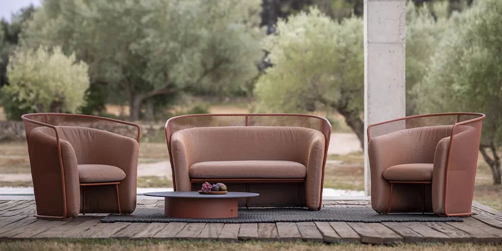 Todus Kollektionen, braune Outdoor-Möbelgarnitur auf Holzterrasse vor grüner Landschaft, bestehend aus Sofa, zwei Sesseln und Tisch.
