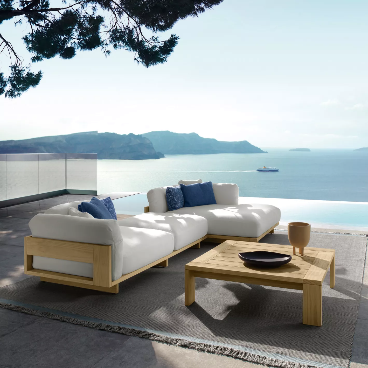 Talenti Argo Loungesofa in Weiß auf Terrasse mit Meerblick, begleitet von einem Holztisch, in entspannter Urlaubsatmosphäre.