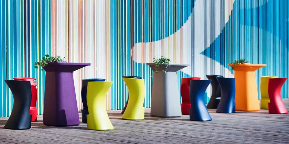 Bunte Vondom Noma Essgruppe aus Kunststoff auf Holzterrasse vor gestreifter Wand, bestehend aus Tischen und Stühlen in verschiedenen Farben.