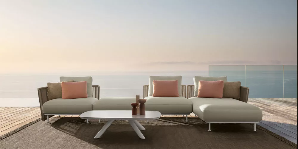 Talenti Coral Kollektion in Beige und Koralle auf einer Terrasse mit Meerblick, bestehend aus modularen Sofas und einem weißen Couchtisch.