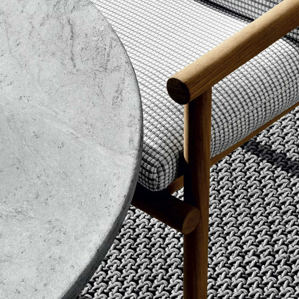 B&B Italia Ayana Esstisch mit grauer Steinplatte und Holzgestell neben einer Bank mit kariertem Polster auf einem geflochtenen Teppich