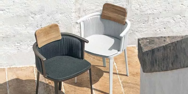 Zwei Ethimo Nicolette Outdoor-Essstühle in Schwarz und Weiß auf einer Terrasse mit Steinboden und weißer Wand im Hintergrund.