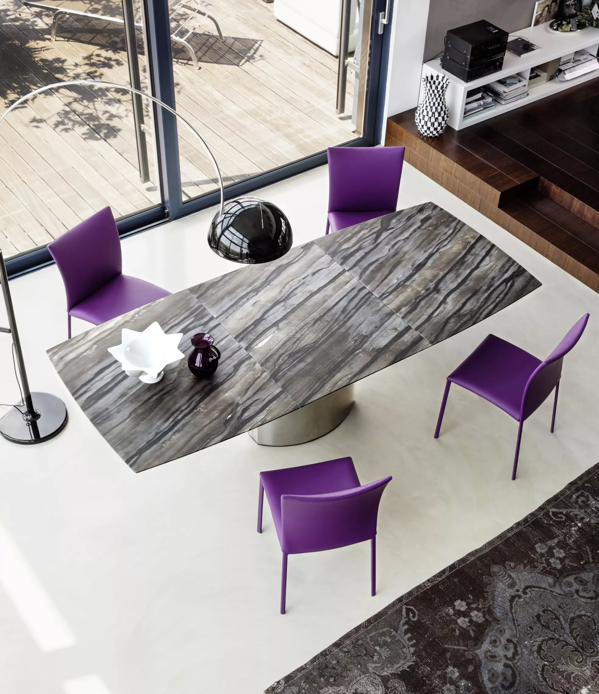 DRAENERT Nobile Soft Esstisch mit vier lila Stühlen in einem modernen Wohnzimmer mit großen Fenstern und Blick auf eine Terrasse
