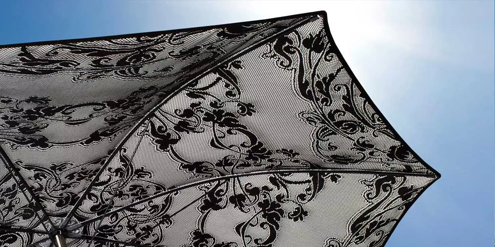 Schwarzer Sywawa Cache-Cache Sonnenschirm mit floralem Muster vor blauem Himmel, Detailansicht der Stoffstruktur.