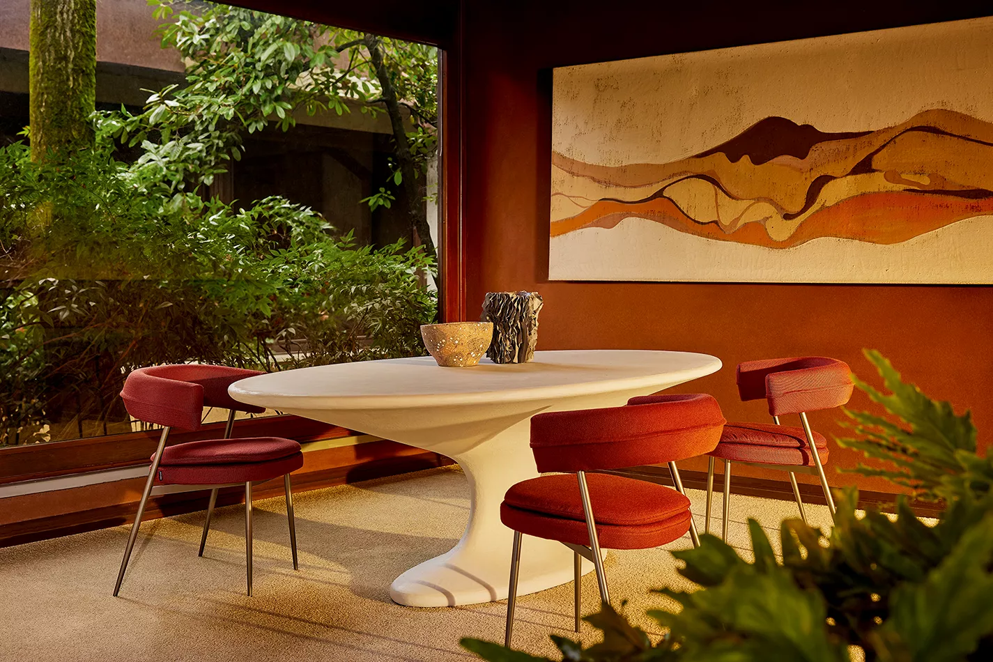 Zanotta Tavolo Fenice in einem stilvollen Esszimmer mit roten Stühlen und Kunstwerk an der Wand im Hintergrund umgeben von Pflanzen.