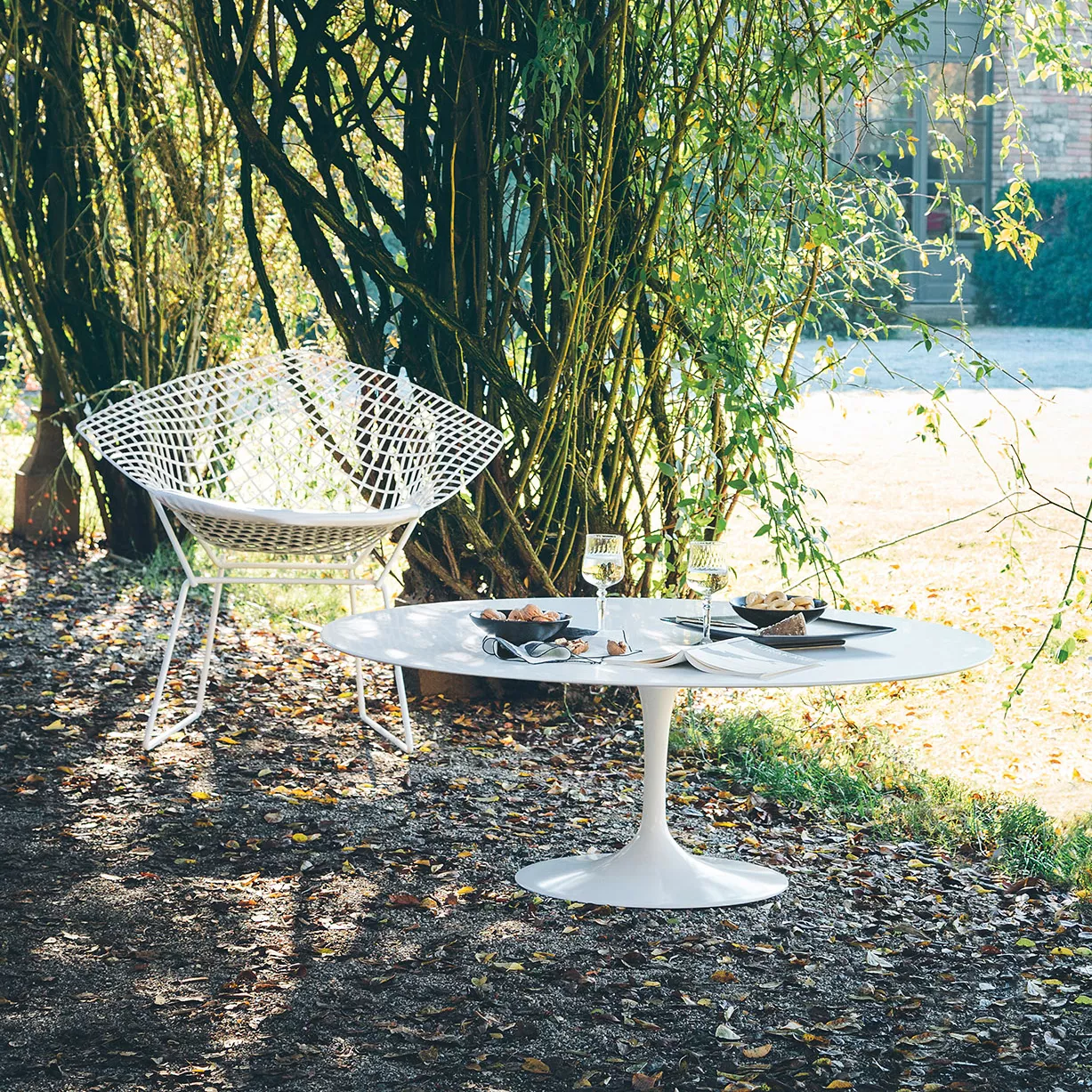 Knoll Harry Bertoia Diamond Chair steht neben einem gedeckten weißen Tisch im Freien unter Bäumen und Sonnenlicht